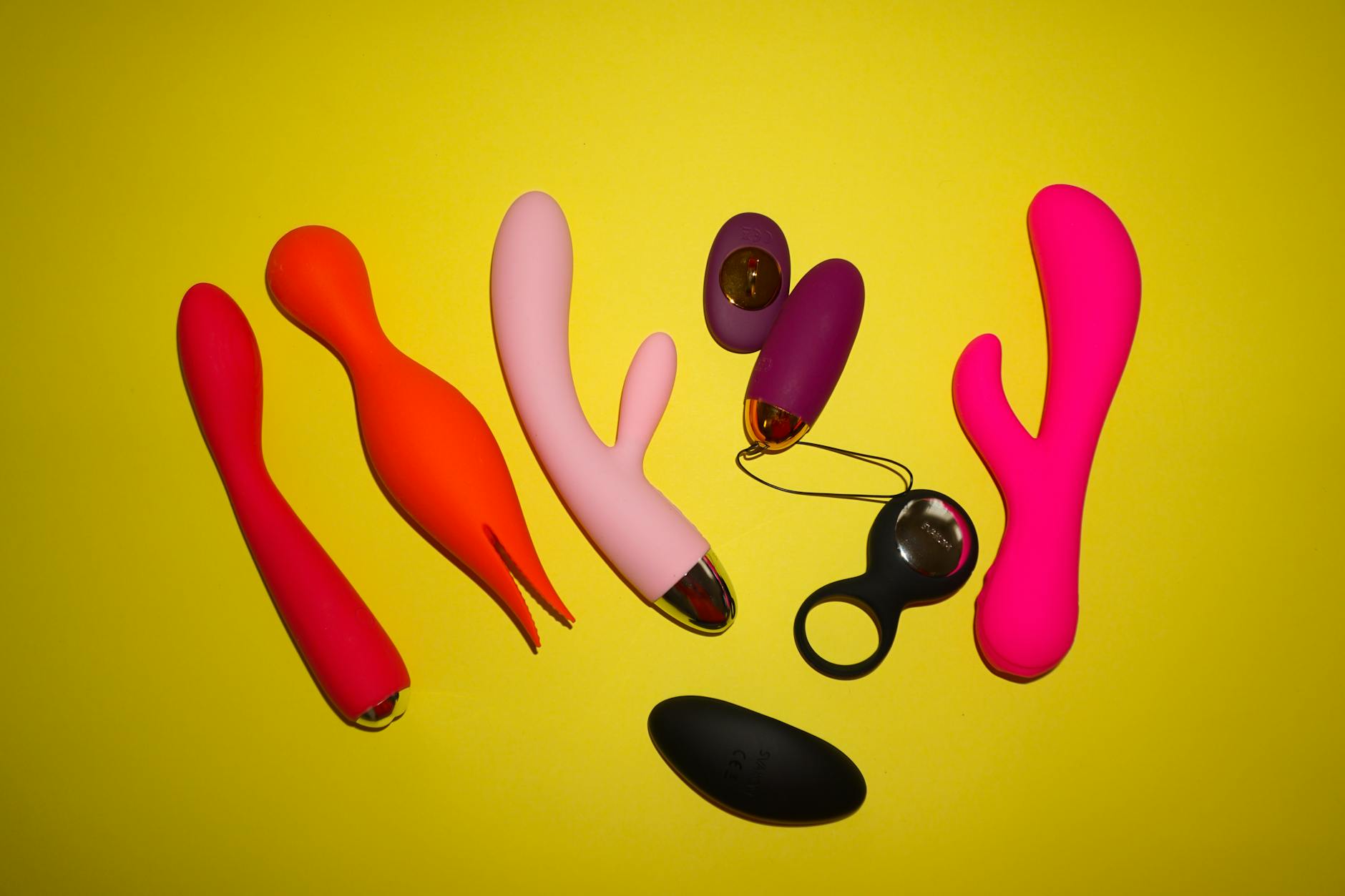 Colorful clitoral vibrators displayed on a bright yellow background, showcasing various designs and pleasure tools