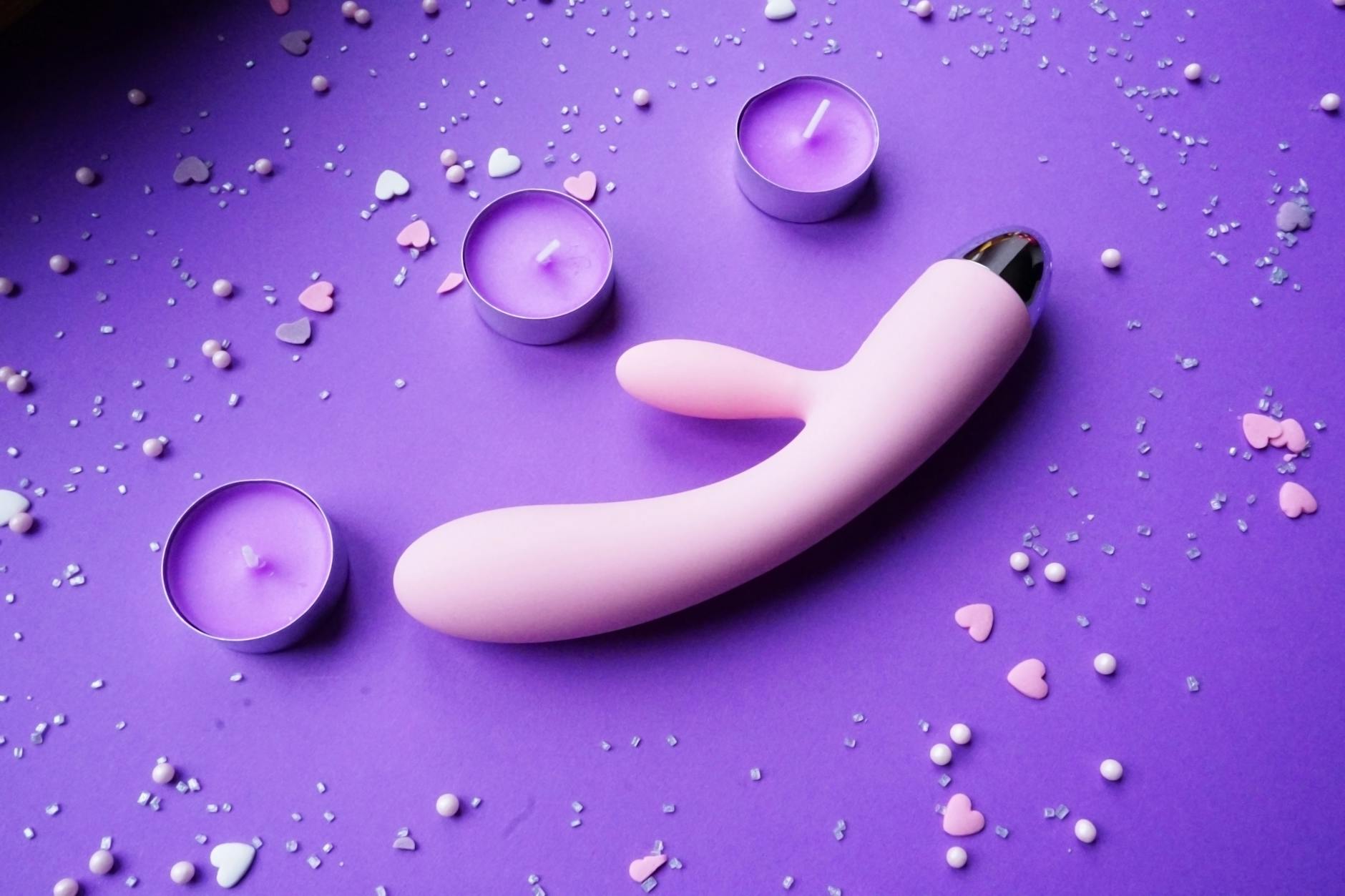 Hand holding a lemon clitoral vibrator against a minimalistic purple backdrop