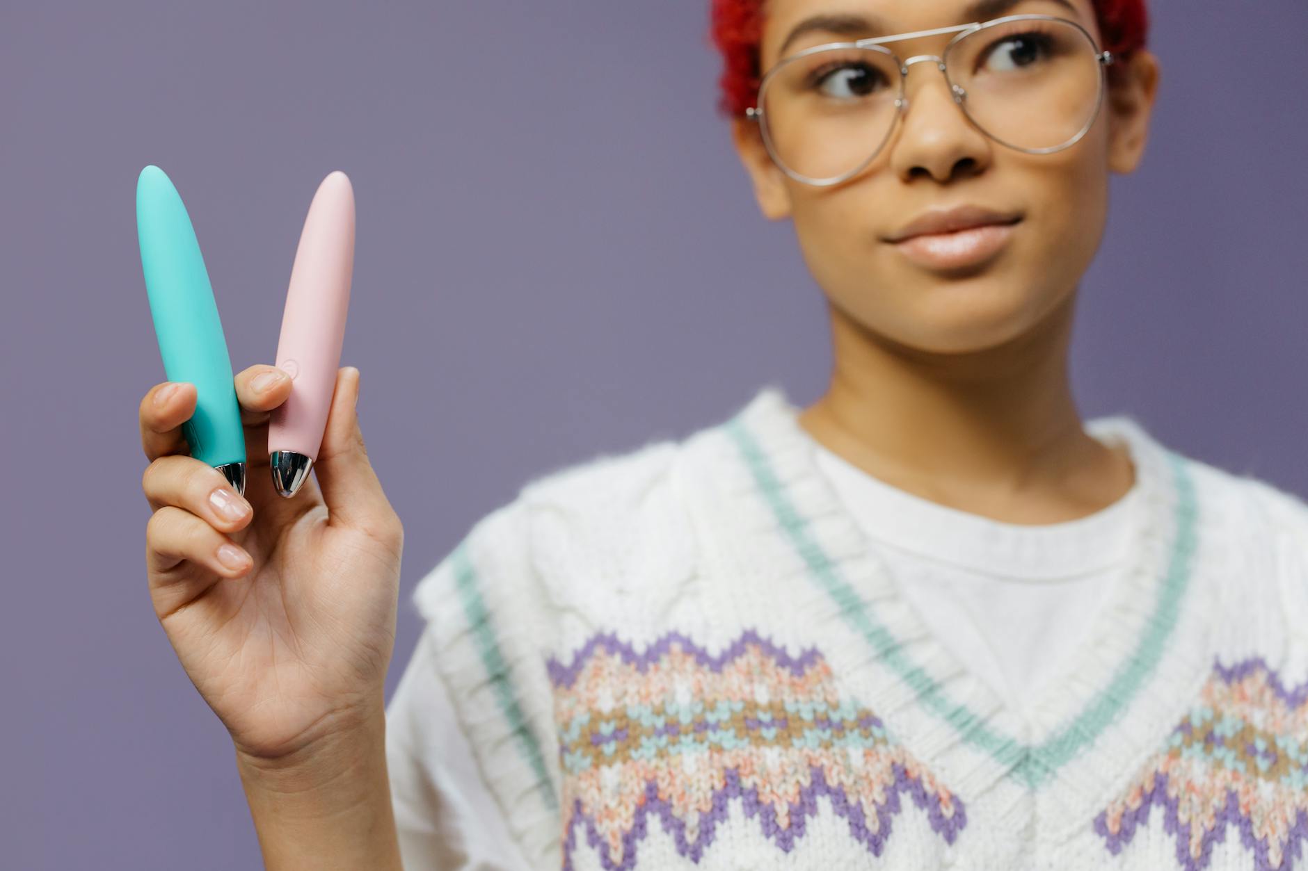 Mujer sosteniendo dos vibradores coloridos contra fondo púrpura, representando variedad y experimentación